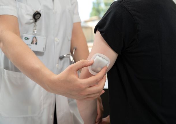 La pompe, similaire à un pansement adhésif, est en train d'être placée sur le bras d'un patient. Ce dispositif médical permet de délivrer la GnRH de façon pulsatile en sous-cutané © 2022 CHUV Éric Deroze